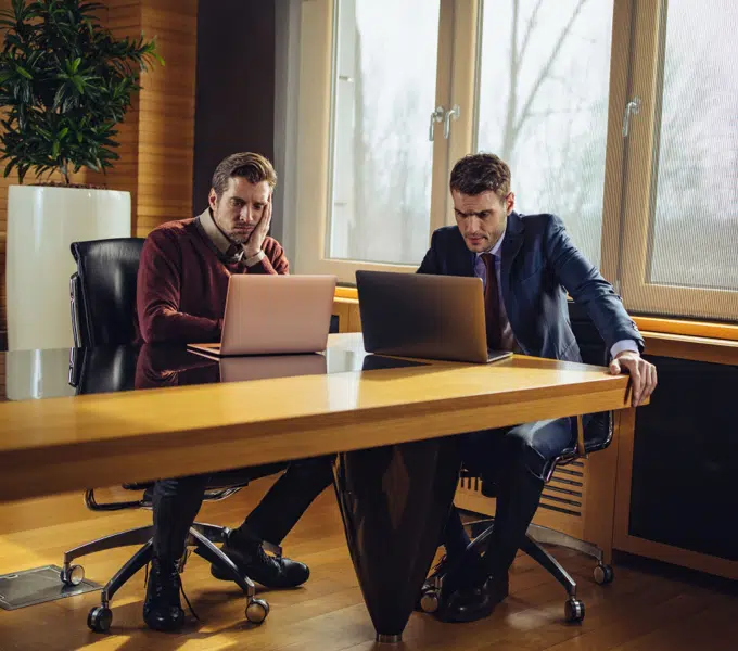 Two professionals working on laptops at a conference table in a modern office