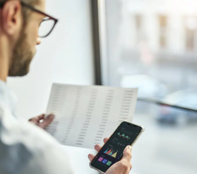 Business professional reviewing data on a smartphone and paper document