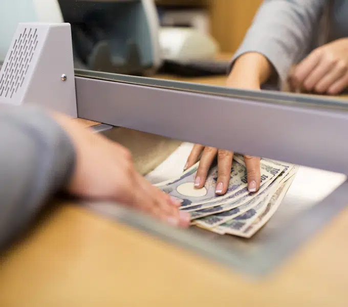 Close-up of hands exchanging U.S. dollar bills across a bank teller counter