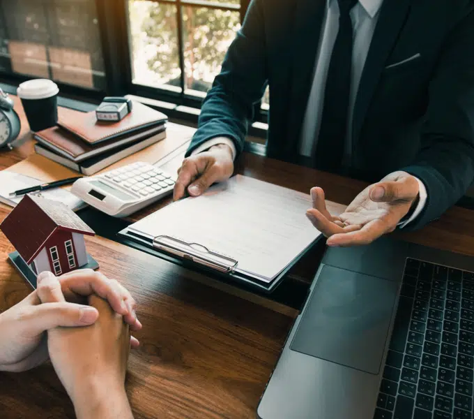 Insurance agent discusses paperwork with a client while reviewing documents at a desk