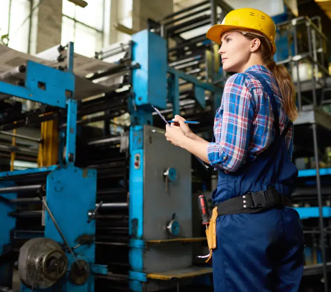 Factory worker in safety gear checks industrial equipment inside a manufacturing plant